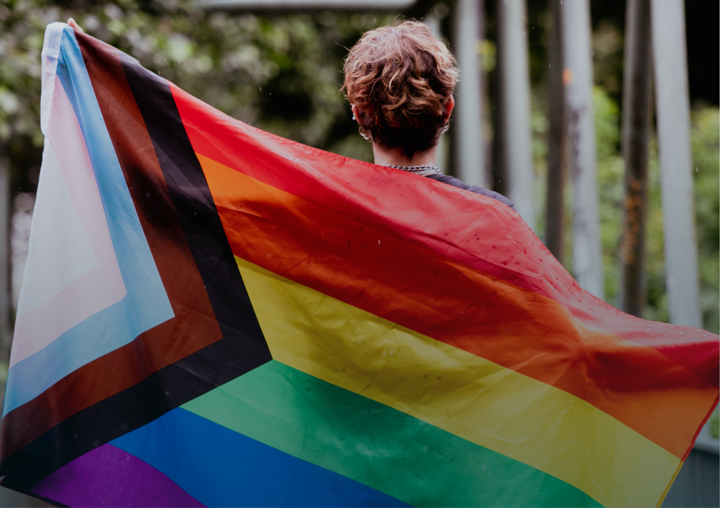 An image of a person holding a LGBTQ Pride flag with text that reads ‘Share Your Pride.’