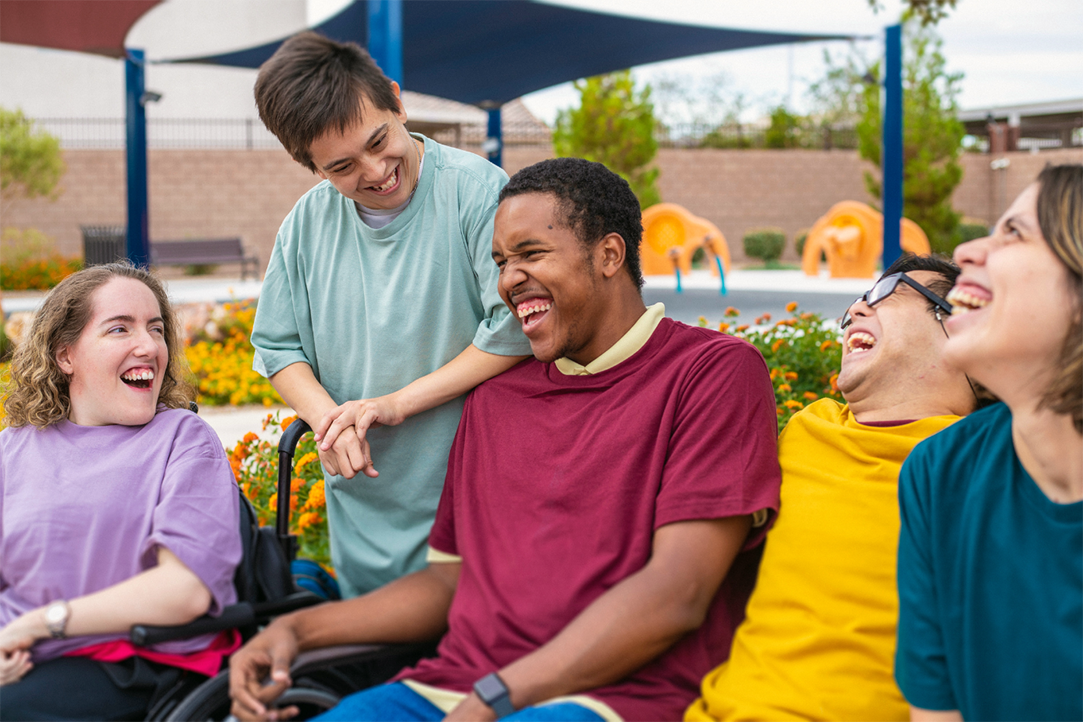 Sessão STEPS2: Cinco jovens com diferentes géneros e deficiências riem juntos num parque.