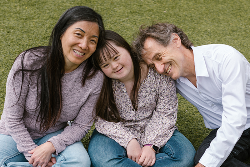 A mother sits next to her daughter who has Down syndrome and her father is at her other side.