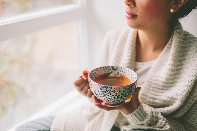 Recovery through Care Management: A woman holds a cup of tea in two hands while looking out a window.