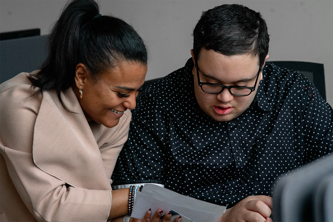 Social Care Network: A woman consults a paper with a young man who has a disability.